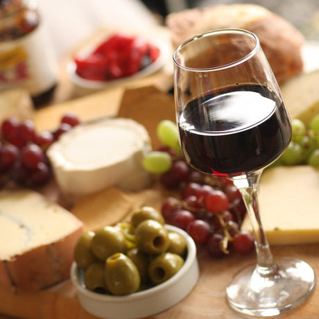 Platter of cheese, olives and grapes with a glass of wine