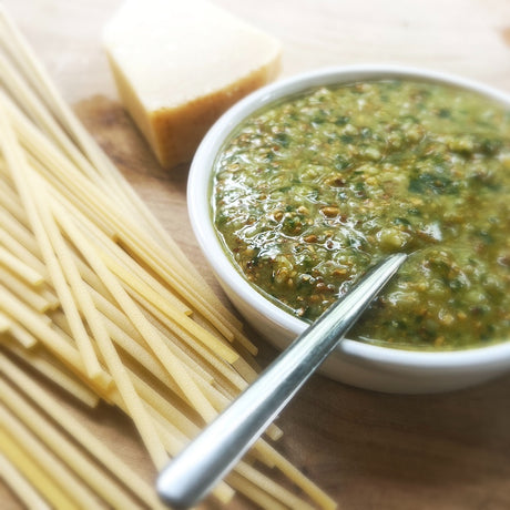 A bowl of smoked pesto with dried pasta & a block of Parmesan cheese