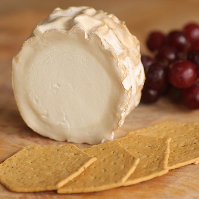 A piece of The Artisan Smokehouse's smoked goats cheese on cheese board with crackers and grapes