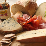 A piece of The Artisan Smokehouse's smoked Stilton on a cheese and smoked meat platter with bread and chutney